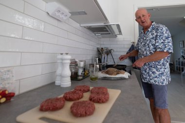A middle-aged man fies  hamburgers in the kitchen.