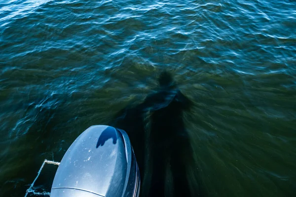 A man\'s shadow is projected into the water over an outboard engine.