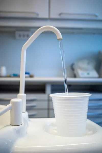 A water dispenser and a water spout next to a dentist\'s chair.