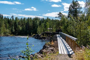 Umea, Sweden A wood walkway over stones along a small creek with rapids.