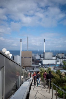 Kopenhag, Danimarka. Amager Bakke enerji santralinin merdivenlerinden çıkan insanlar alp kayağı ve elektrik santrali manzarası için kayak yamacı olarak ikiye katlanıyor..