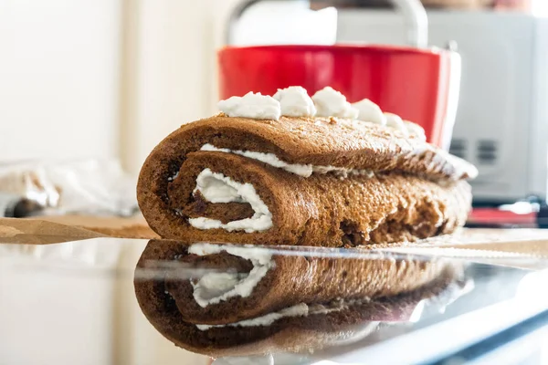 A rolled sponge cake with frosting and its reflection.