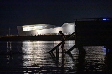 Kopenhag, Danimarka. Bir kişi sabahın erken saatlerinde Öresund 'da Danimarka Ulusal Akvaryumu, Den Blla Gezegeni ve Mavi Gezegen' in önünde yıkanır..