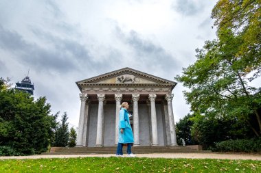 Kopenhag, Danimarka 'da mavi yağmurluklu bir kadın 1805' ten itibaren Frederiksberg Bahçeleri 'nde Apis Tapınağı' nın yanından geçiyor..