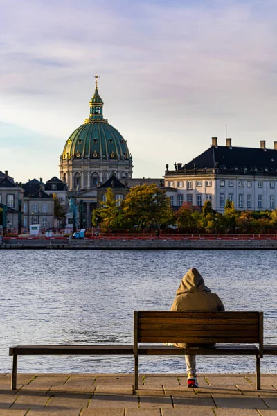 デンマークのコペンハーゲンコペンハーゲン港とフレデリク教会を見下ろすベンチの上に パーカーを着た男が座っている — ストック写真