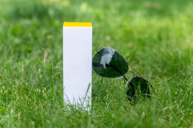 Güneş gözlüğü, tazelik ve gençliğin yanındaki yeşil çimenlerin üzerindeki bir krem tüpünden ambalaj tasarımcısı için paketleme