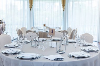 Konuklar gelmeden önce salonda tabaklar ve bardaklarla servis edilen temiz beyaz masa örtüsü olan bir masa.