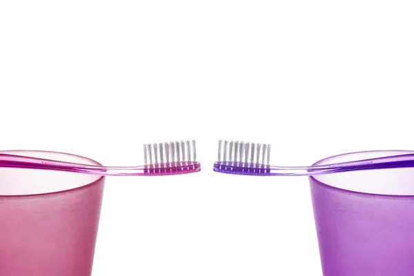 Dos cepillos de dientes púrpura diferentes en las copas de plástico opuestas entre sí sobre fondo blanco — Foto de Stock