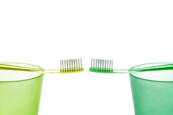 Green and yellow toothbrush on the plastic cups opposite each other on a white background — Stock Photo, Image