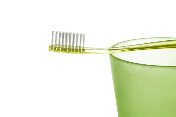 A olive-green plastic toothbrush lies on a green plastic cup on white background — Stock Photo, Image