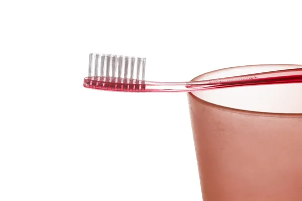 Un cepillo de dientes de plástico rojo se encuentra en una taza de plástico rojo sobre fondo blanco — Foto de Stock