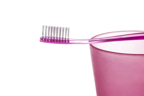 Un cepillo de dientes de plástico púrpura se encuentra en una taza de plástico púrpura sobre fondo blanco — Foto de Stock