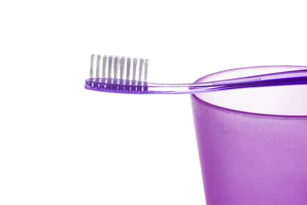 Un cepillo de dientes de plástico púrpura se encuentra en una taza de plástico verde sobre fondo blanco — Foto de Stock