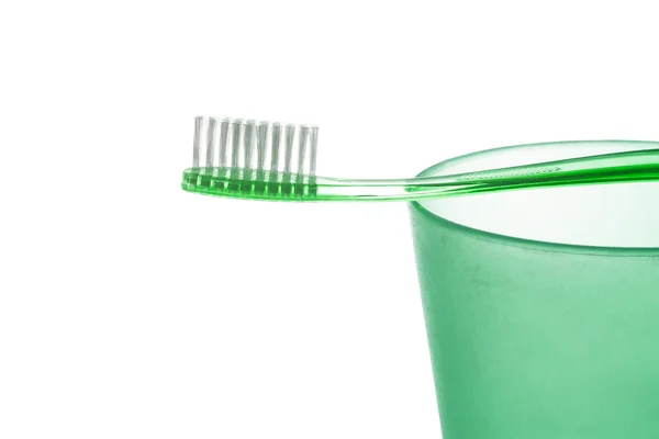 An emerald plastic toothbrush lies on a green plastic cup on white background — Stock Photo, Image