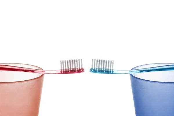 Cepillo de dientes rojo y azul en las copas de plástico opuestas entre sí sobre un fondo blanco — Foto de Stock