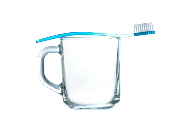 Cepillo de dientes de plástico azul descansa sobre una taza de vidrio transparente sobre blanco — Foto de Stock