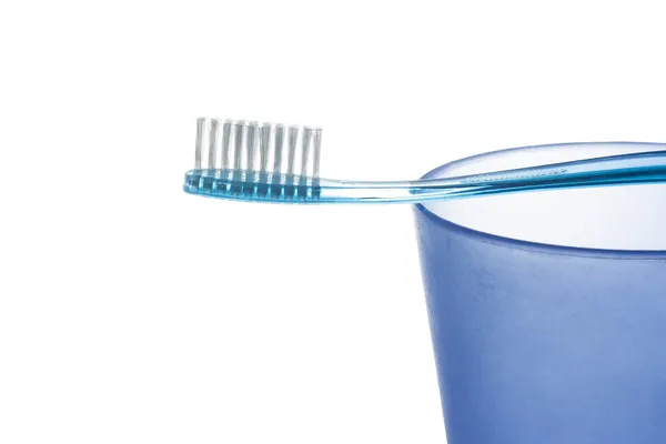 A blue plastic toothbrush lies on a blue plastic cup on white background — Stock Photo, Image