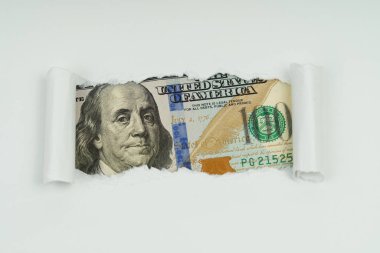İş ve finans kavramı. Bir kağıt parçasının yırtık deliğinde 100 dolarlık bir banknotun görüntüsü görünür.