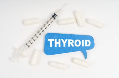 Tıp ve sağlık konsepti. Beyaz arka plan hapları, bir şırınga ve üzerinde THYROID yazan mavi bir plaka.