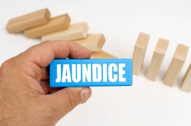 Tıp ve sağlık konsepti. Arka planda tahta tahtalar var. Yarısı ayakta, yarısı yalan söylüyor. Üzerinde JAUNDICE yazan mavi bir plaketin ellerinde.