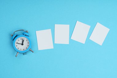 Mavi arka planda, bir çalar saat ve beyaz kağıt parçaları. Model