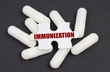 Tıp konsepti. Siyah bir arkaplanda, kapsüller ve yazılı bir bulmaca - IMMUNIZATION
