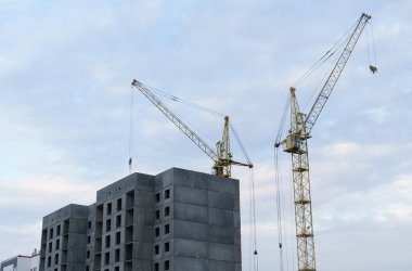 İnşaat konsepti. Gökyüzünün arka planında yapım aşamasında olan çok katlı bir bina ve iki vinç var.