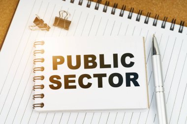 Ekonomi ve iş kavramı. Masanın üzerinde bir kalem, kıskaç ve üzerinde PUBLIC SECTOR yazan bir defter var.