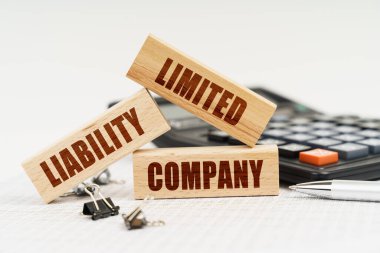 İş ve Ekonomi. Masanın üzerinde bir kalem, bir hesap makinesi ve yazılı küçük tahta bloklar var. LiMITED LIABILITY COMPANY