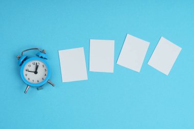 Mavi arka planda, bir çalar saat ve beyaz kağıt parçaları. Model
