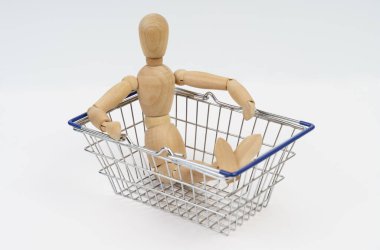 İş konsepti. Tahta adam bir alışveriş sepetinde oturur. Beyaz arkaplanda izole.