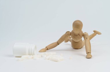 İlaç ve bağımlılık konsepti. Tahta adam haplar için sürünüyor. Beyaz arkaplanda izole.