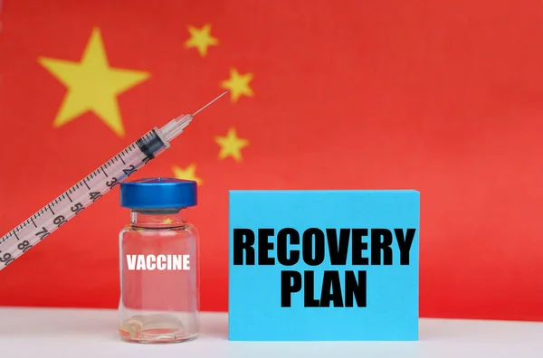 Medicine concept. Vaccine, syringe and blue plate with the inscription - RECOVERY PLAN. In the background the flag of China