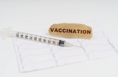 Masanın üzerinde bir kardiyogram, bir şırınga ve yazılı bir kağıt var.