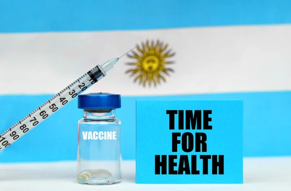 Impfstoff, Spritze und blauer Teller mit der Aufschrift - Zeit für Gesundheit. Im Hintergrund die Flagge Argentiniens — Stockfoto