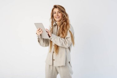 Bir kadın blogcu elinde bir tablet tutuyor, diğer eliyle sayfaları hazırlıyor. Çerçeveye bakıyor..