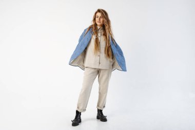 Bir kadın ellerini cebinde tutar, ceketinin düğmeleri açıktır, yana bakar, gülümser..