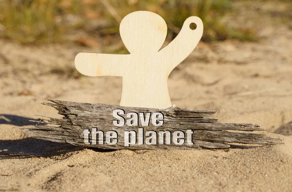 På sanden nära träfiguren av en man finns en träbit med inskriptionen - Save The Planet — Stockfoto