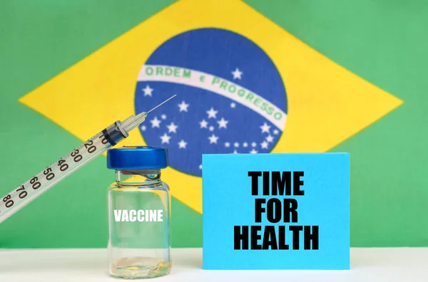 Impfstoff, Spritze und blauer Teller mit der Aufschrift - Zeit für Gesundheit. Im Hintergrund die Fahne Brasiliens — Stockfoto