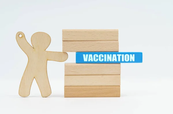 Eine menschliche Figur schiebt einen blauen Holzblock mit der Aufschrift VACCINATION von einer Wand aus Blöcken. — Stockfoto