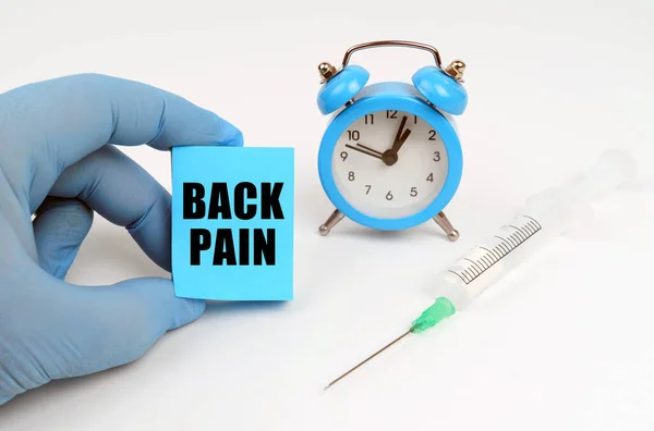 On the table is a syringe and an alarm clock, in his hand a notebook with the inscription - BACK PAIN — Stock Photo, Image