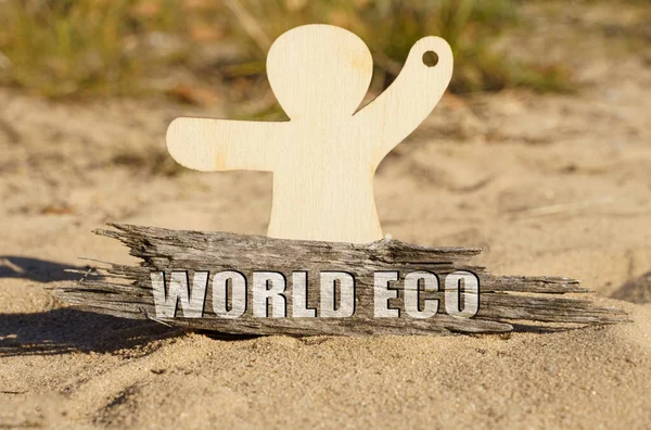 Op het zand bij het houten beeldje van een man staat een stuk hout met de inscriptie - WORLD ECO — Stockfoto