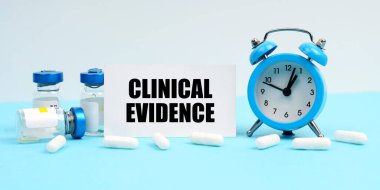 Tıp ve sağlık konsepti. Bir çalar saat, haplar, iğneler ve üzerinde klinik kanıt yazan bir kart.