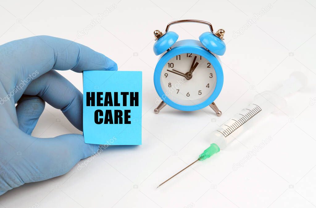 Medicine concept. On the table is a syringe and an alarm clock, in his hand a notebook with the inscription - HEALTH CARE