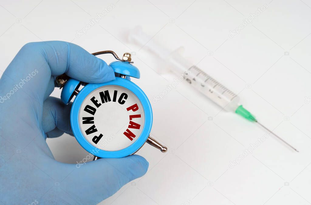 Medicine concept. There is a syringe on the table, an alarm clock in his hand with an inscription on the scoreboard - PANDEMIC PLAN