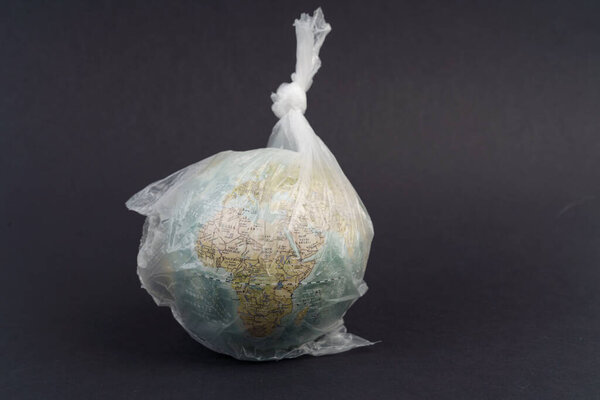 Экологическая концепция охраны окружающей среды. Стеклянный шар в пластиковом пакете на черном фоне. Спасти планету