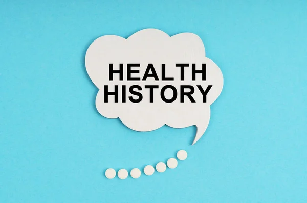 On a blue table are pills and a white plate with the inscription - HEALTH HISTORY — 图库照片