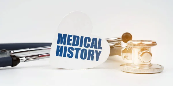 On the white surface there is a stethoscope and a heart plate with the inscription - MEDICAL HISTORY — 图库照片