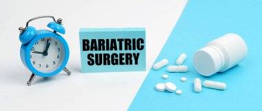 On a blue surface are pills, on a white surface an alarm clock and a plate with the inscription - bariatric surgery