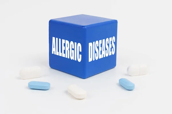 On a white surface are pills and a blue cube that says - Allergic diseases — Zdjęcie stockowe